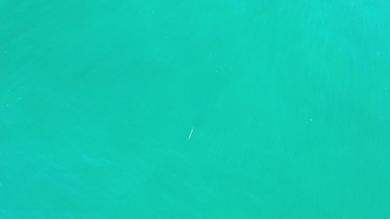 Top-down Los Cabos ocean frame with smooth green water, faint submerged tonal patches, small white wave lines, and no visible people.