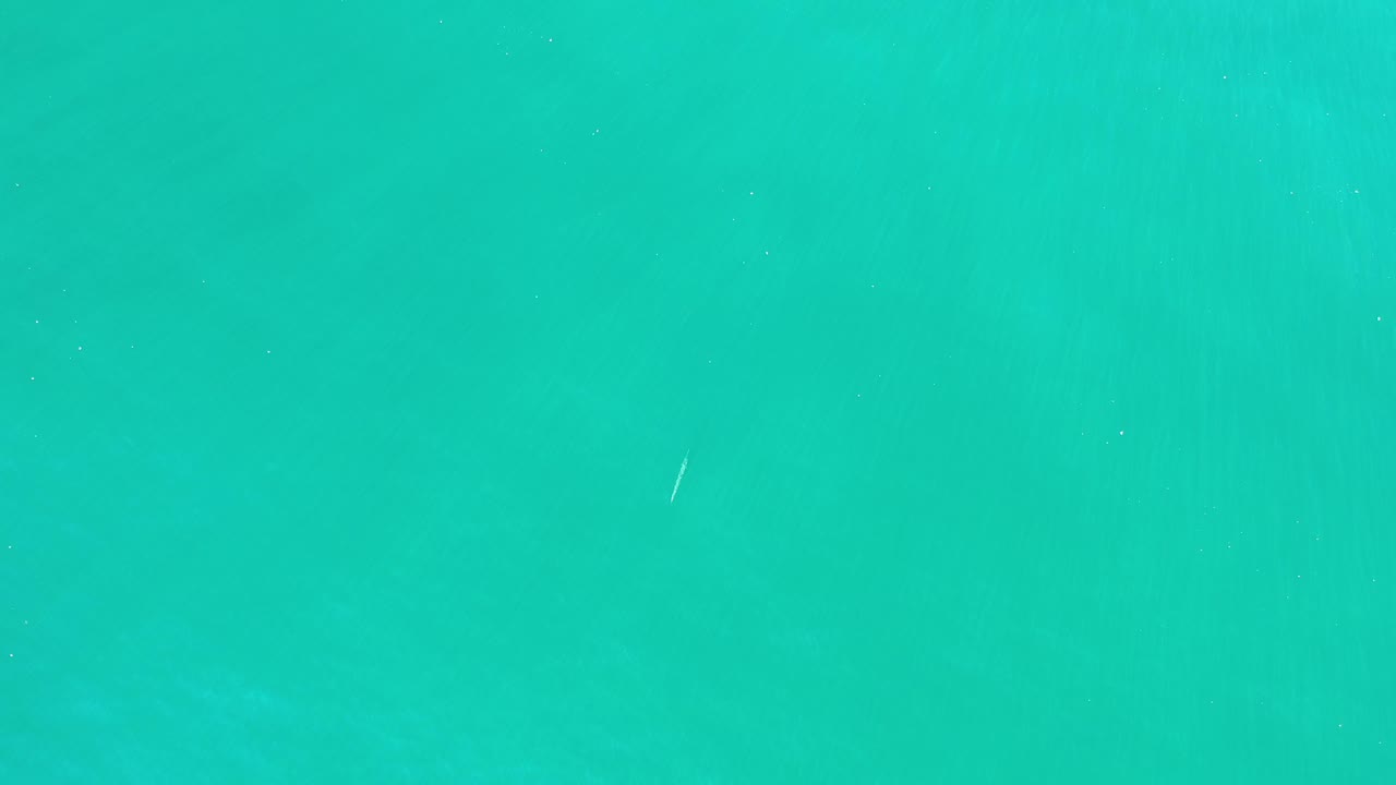 Aerial green water surface with isolated white wave traces.