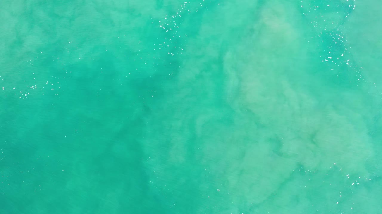 Overhead view of teal-blue water in Los Cabos, Mexico, with pale cloudy swirls beneath the surface and no visible people.
