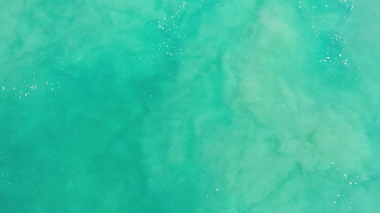 Turquoise sea surface in Los Cabos, Mexico, showing mottled pale-blue patterns and scattered white sparkle points, with no visible people.
