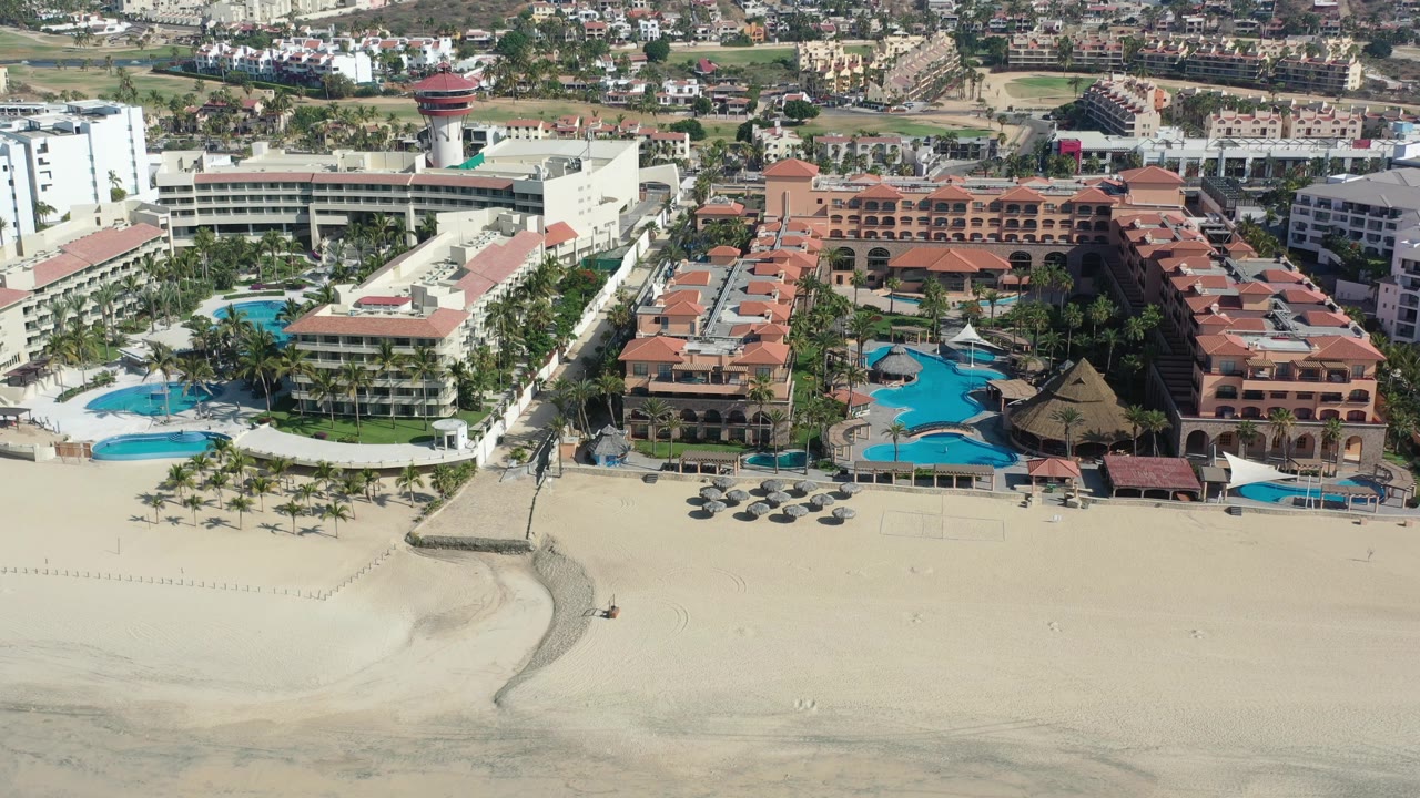 Aerial resort frontage with beach, pools, palms, and surrounding city blocks.