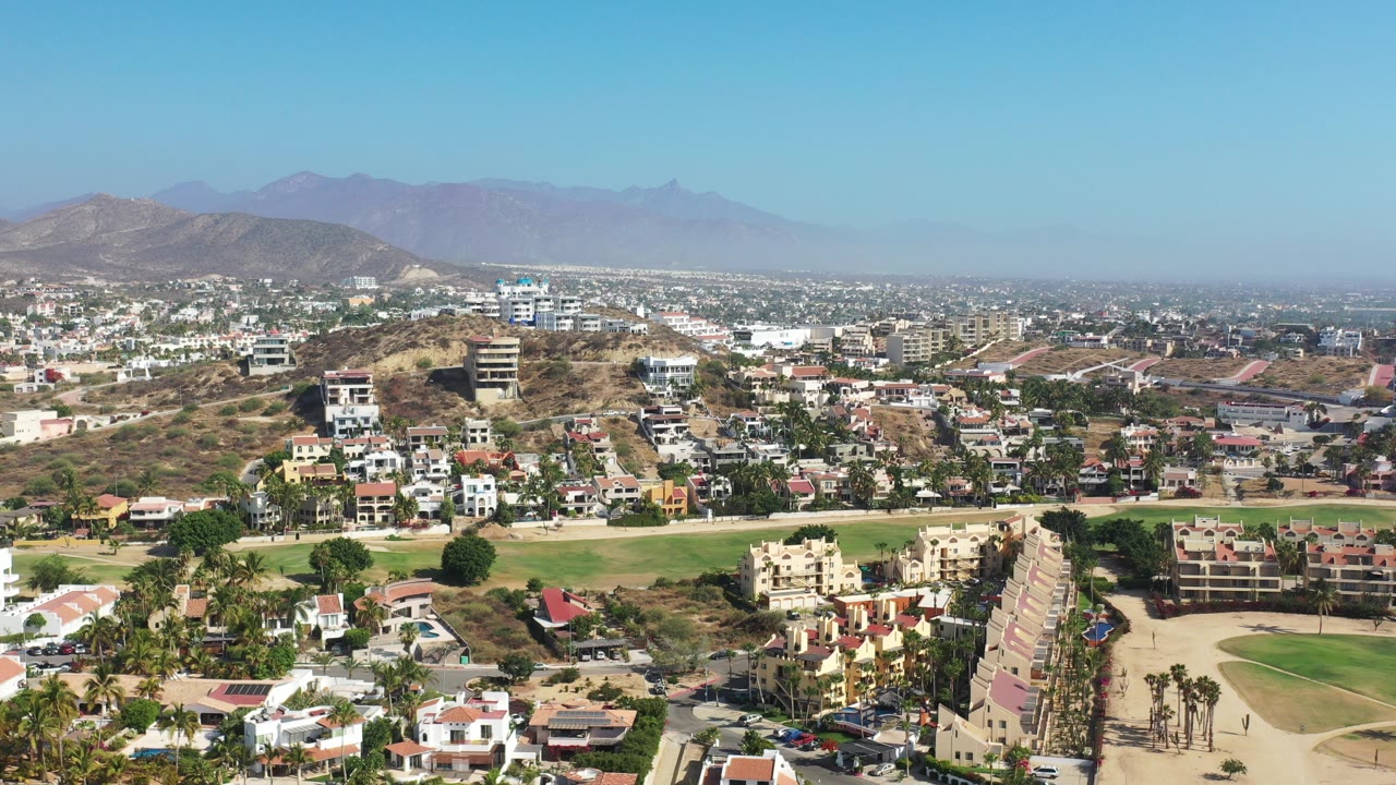 Elevated view of Los Cabos homes, golf greenery, dry hills, and blue sky.
