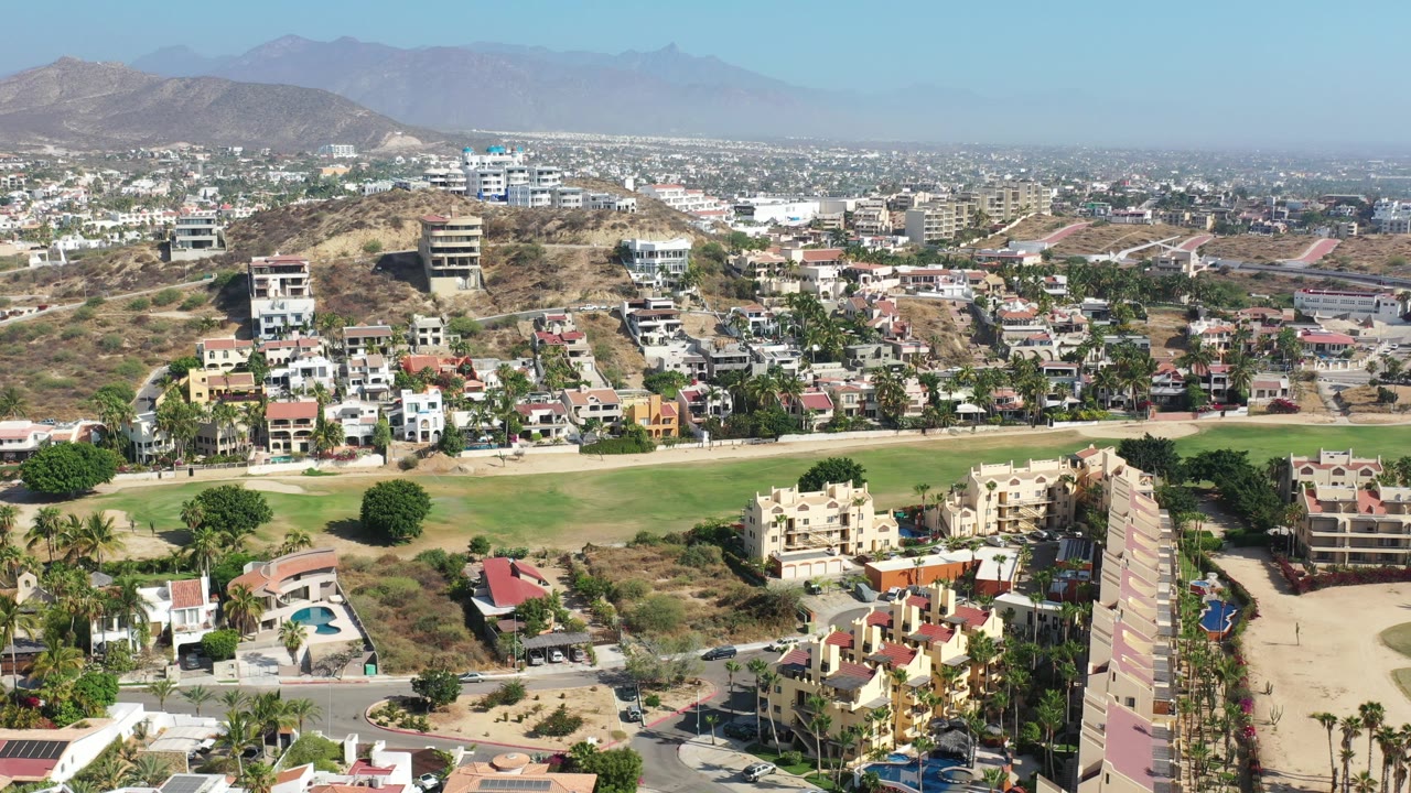 Wide aerial neighborhood view with dry hillside, homes, trees, and mountains.