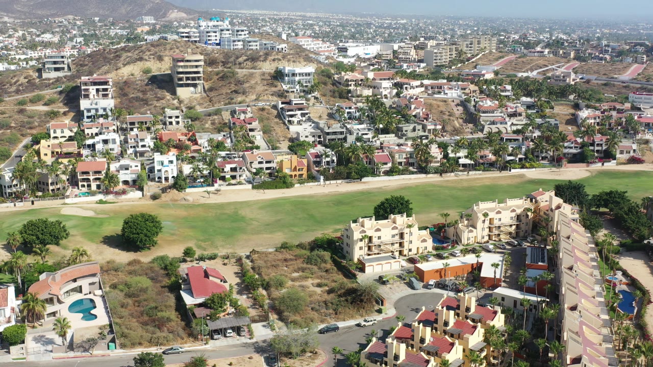 Aerial view of hillside homes beside a green field and roads.