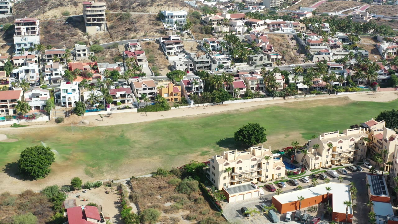 Aerial view of villas beside a green course and hillside homes.