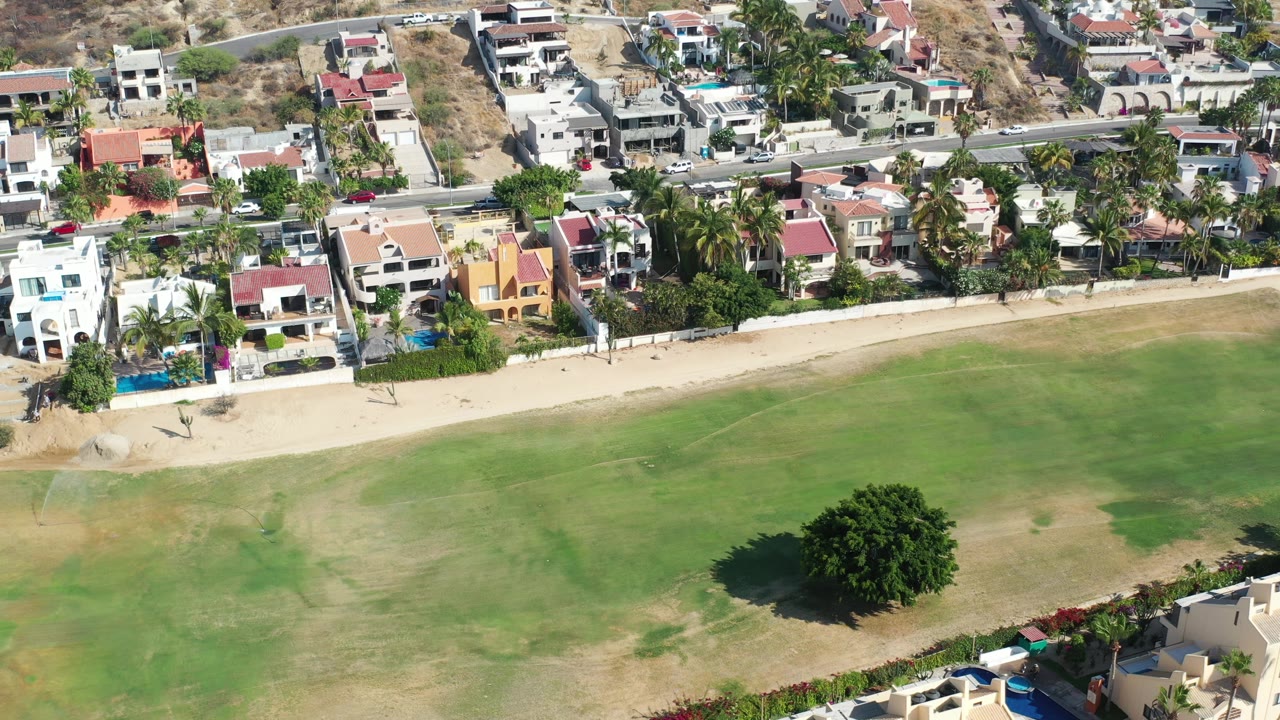 Aerial view of villas, road, sandy strip, and green open land.