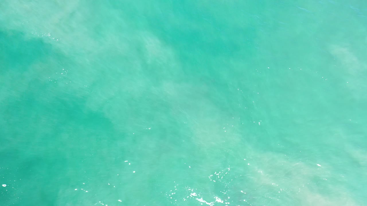 Straight-down view of turquoise ocean water in Los Cabos, Mexico, with pale cloudy wave patterns and no visible people.