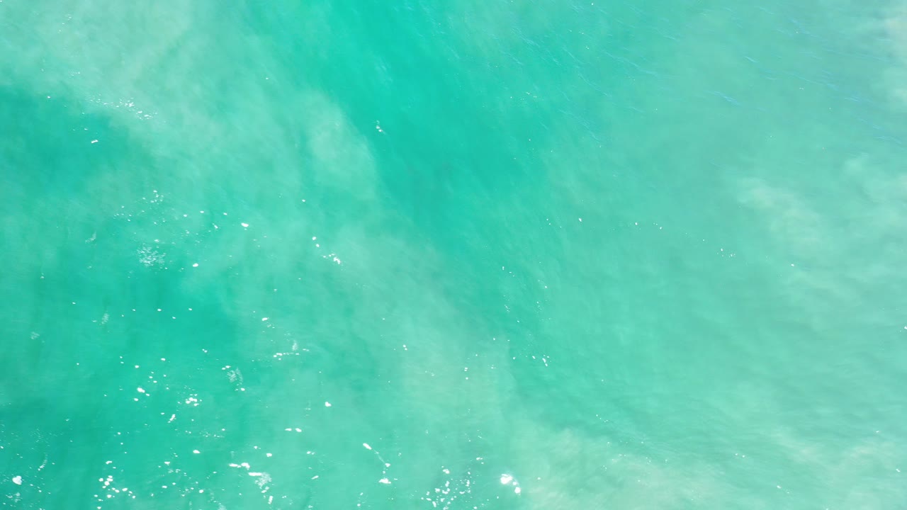 Turquoise ocean water in Los Cabos fills the overhead frame with pale underwater swirls near the upper left and no visible people.