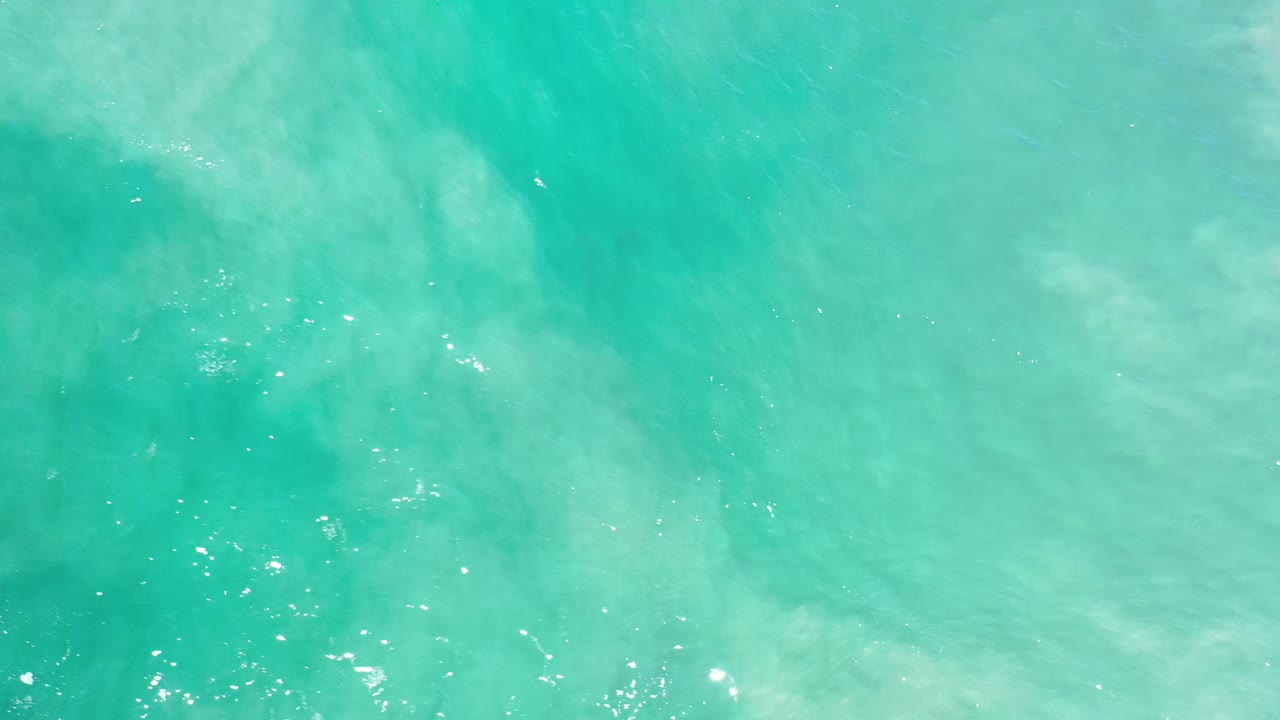 Aqua ocean water in Los Cabos shows soft cloudy shapes beneath the surface, small ripples, and no visible people.