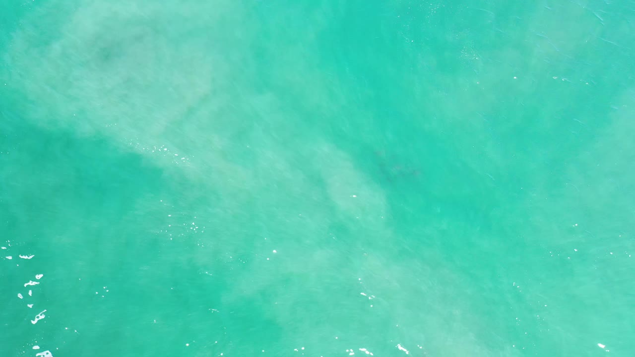 Green ocean surface in Los Cabos, Mexico, seen from above with broad pale patches under the water and no visible people.