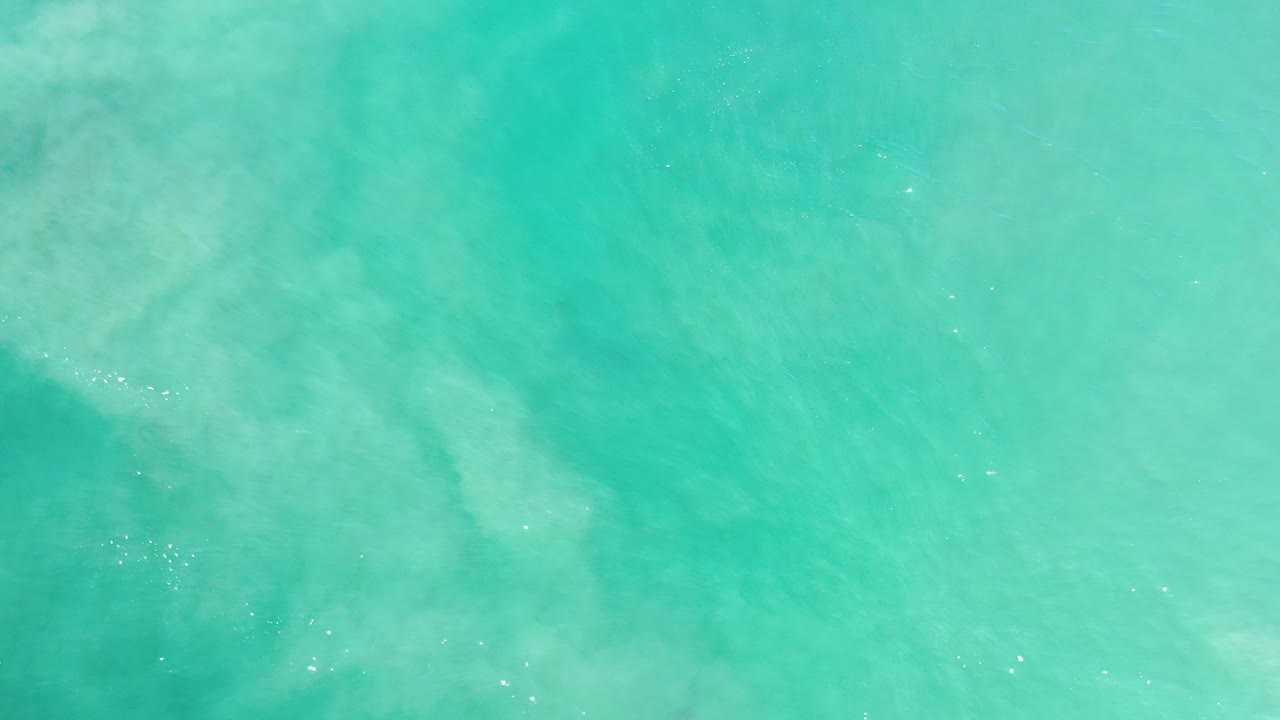 Overhead view of turquoise water in Los Cabos, Mexico, with pale submerged patches, light surface texture, and no visible people.