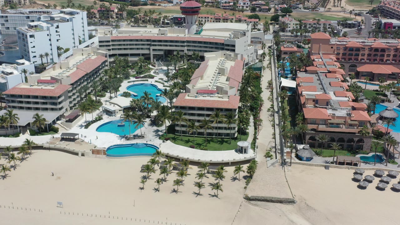 Aerial view of beachfront buildings, pools, palms, and sand.