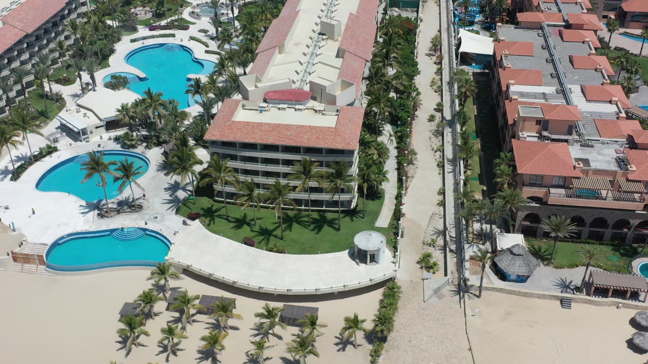 Aerial view of beachside pools, palm trees, and red roof buildings.