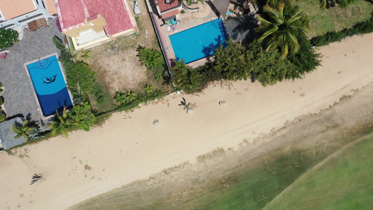 Overhead view of beach houses, pools, palms, sand, and shallow water.