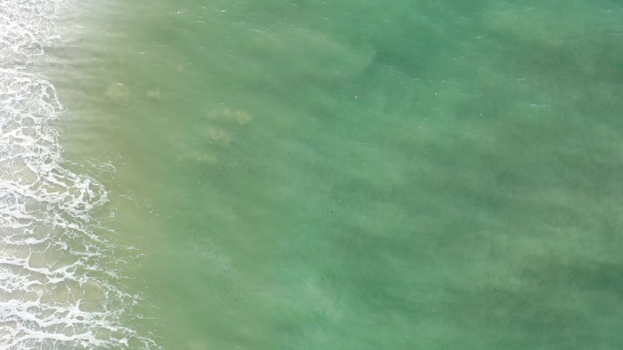 Overhead view of green-blue ocean in Los Cabos, Mexico, with white foam brushing the left edge and no visible people.