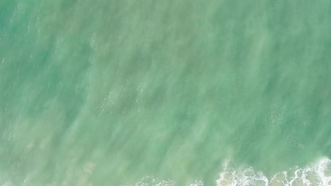 Top-down ocean water with soft green tones and foamy waves near the bottom.