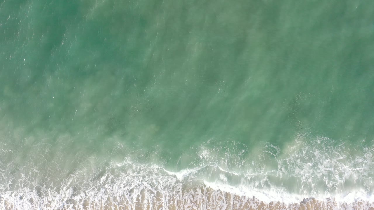 Overhead turquoise surf breaking along a sandy shore