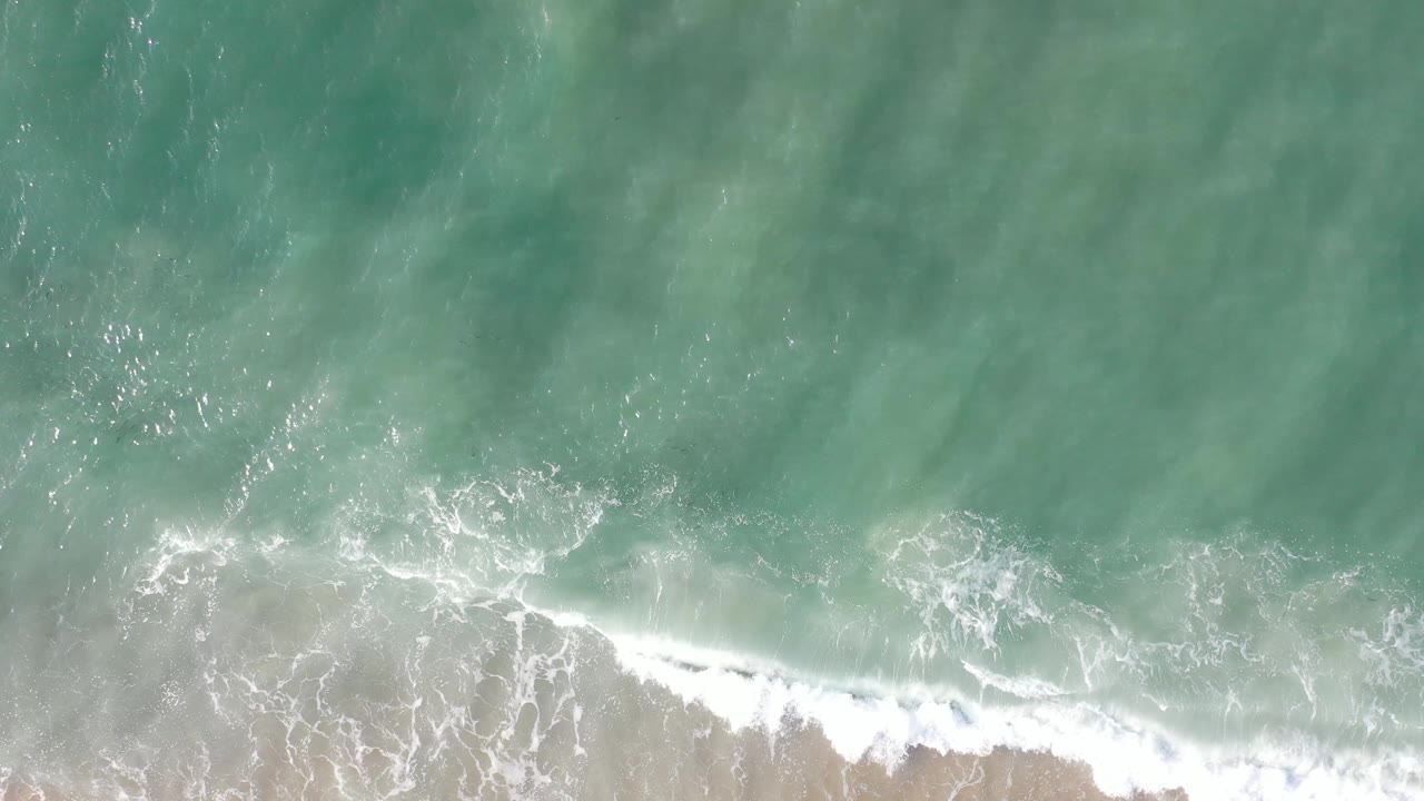 Green ocean water and breaking white wave on sand