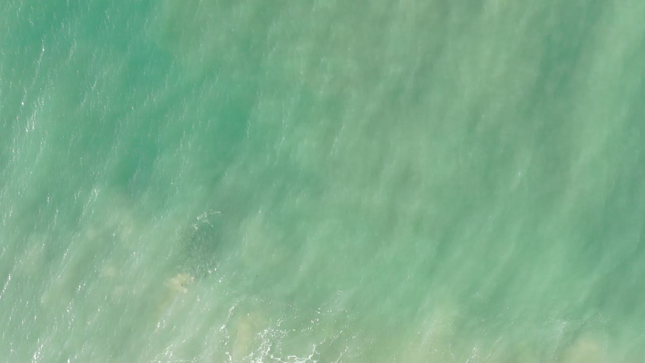 Overhead view of turquoise Los Cabos seawater with pale sand showing through and no visible people at the start of the clip.
