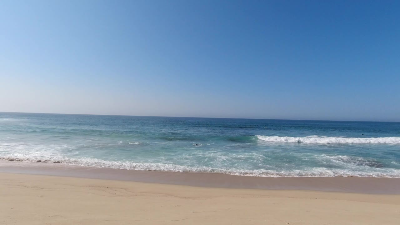Wide beach view with waves, sand, rocks, and blue sky