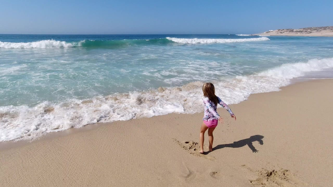 Young girl standing on sand near incoming ocean surf.