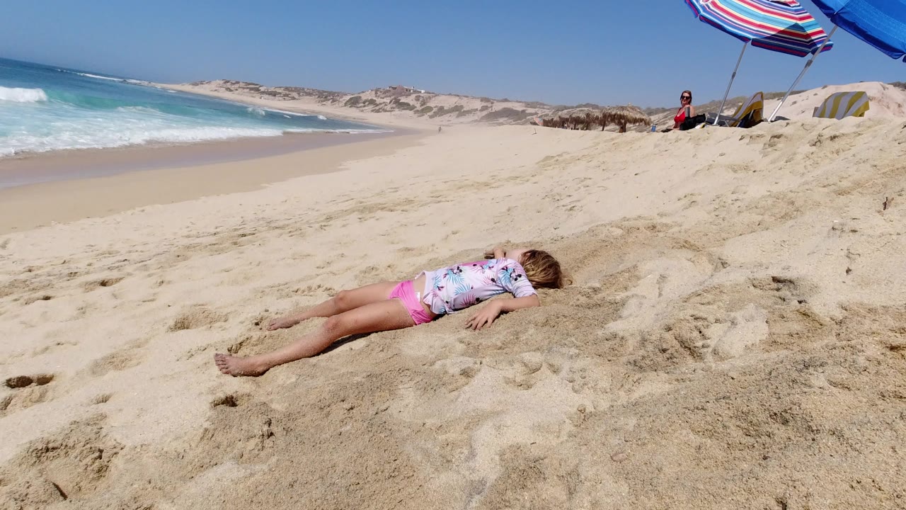 Small child lying on sand beside a bright beach shoreline.