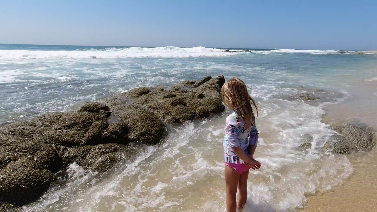 Child standing beside rocky surf on a beach.
