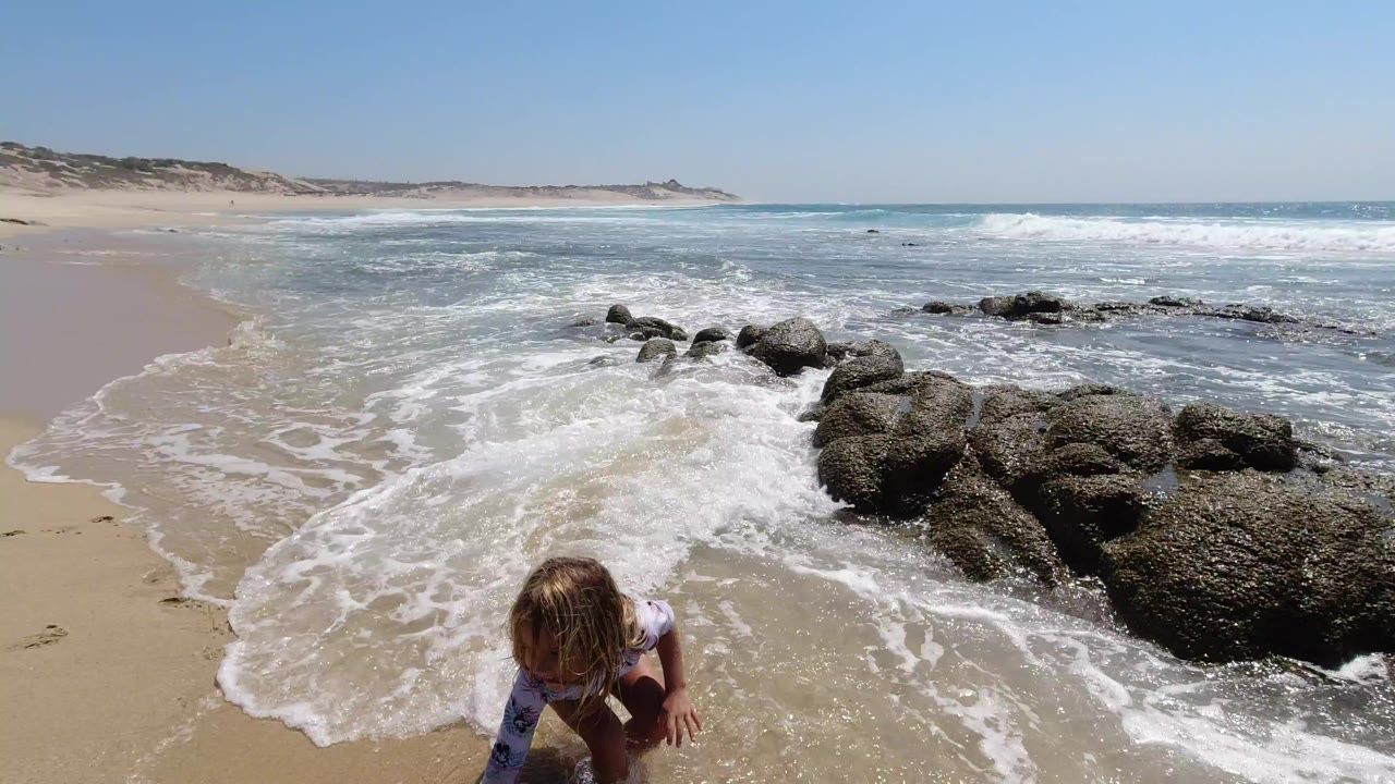 Child crouching near foamy surf and dark shoreline rocks.