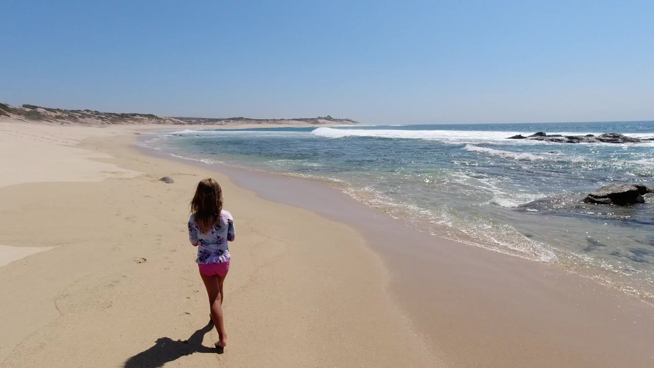 Child walking on a sandy beach toward blue surf.