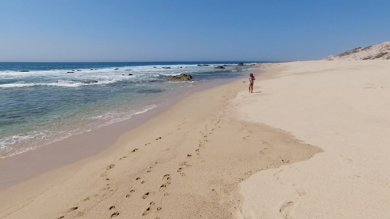 Child walking on a sandy beach beside the ocean.