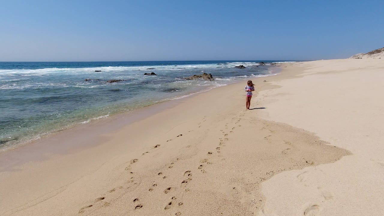 At 0:01, the girl remains near the right side of the waterline as small waves break across the left side of the Los Cabos beach frame.