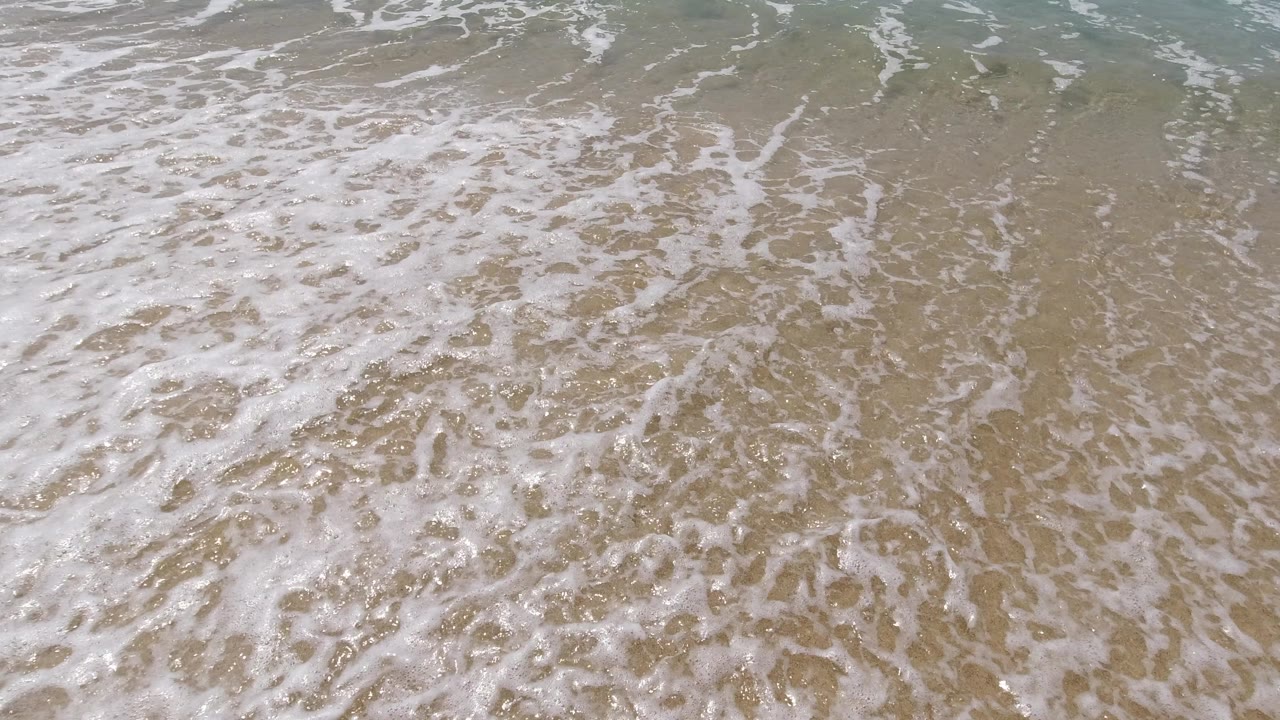 Foamy shallow seawater over tan sand