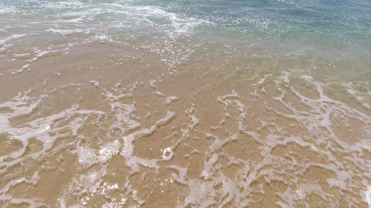 Sea foam forms branching white lines over shallow water on a Los Cabos beach, with no visible people or built structures.