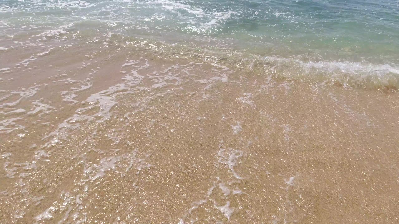 A small wave breaks lightly over clear shallow water.