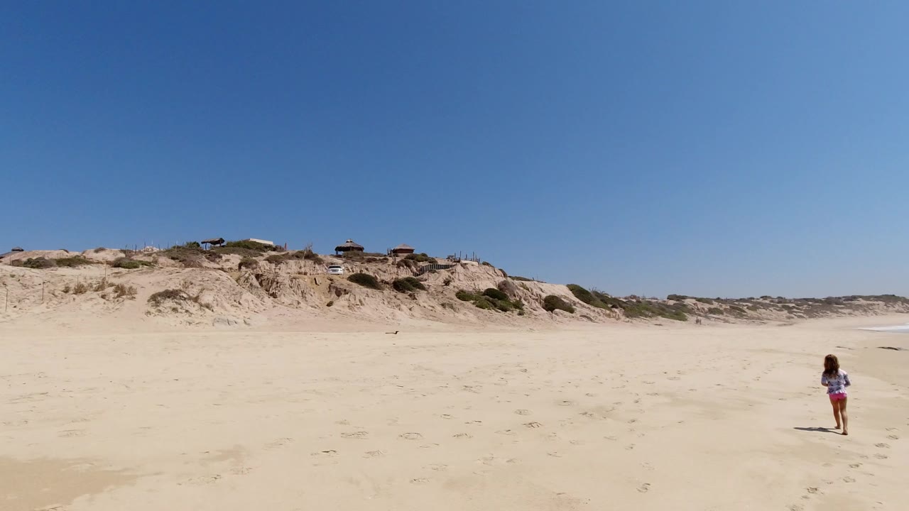 Young girl walking on a wide sandy beach under a blue sky.