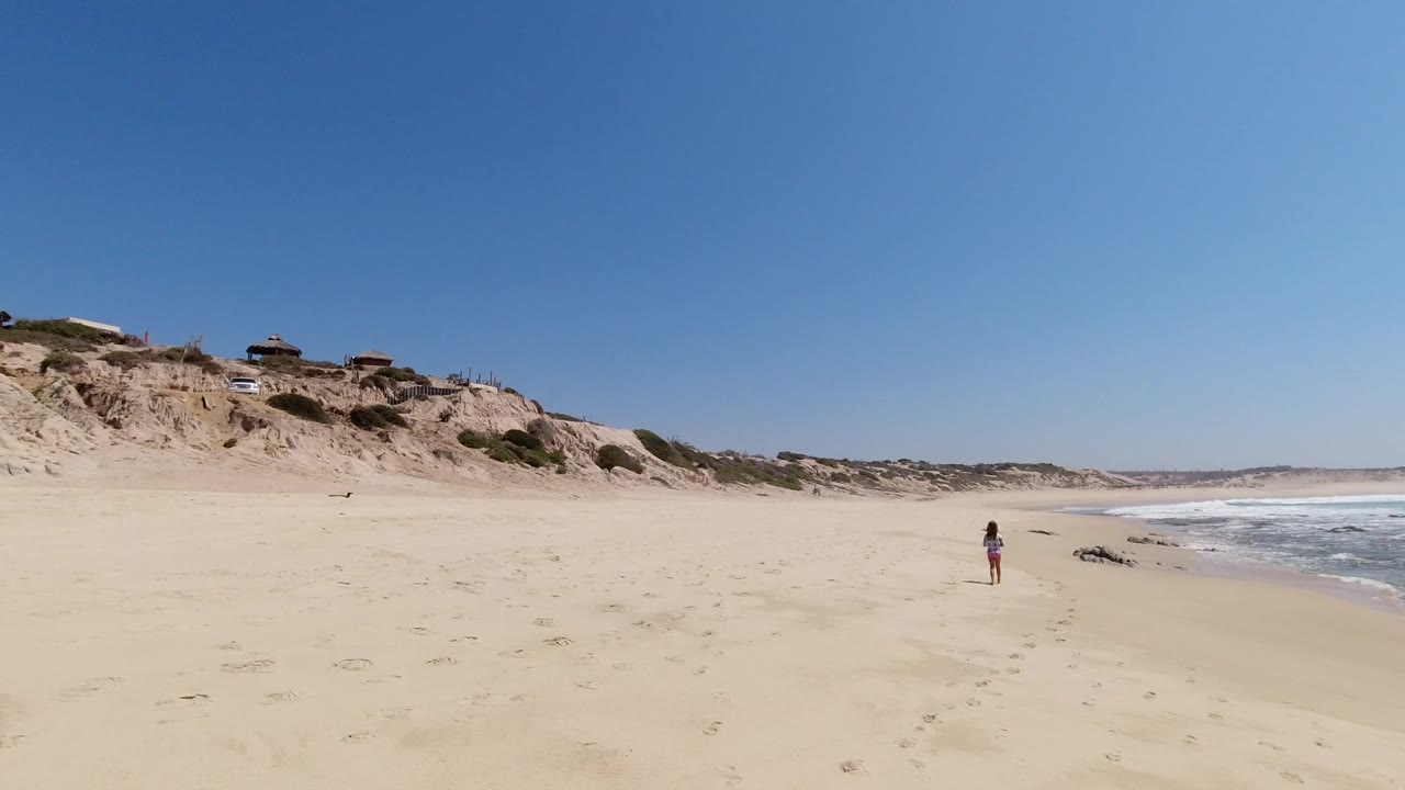 Wide sandy beach with bluffs, seaside homes, surf, and a distant person.