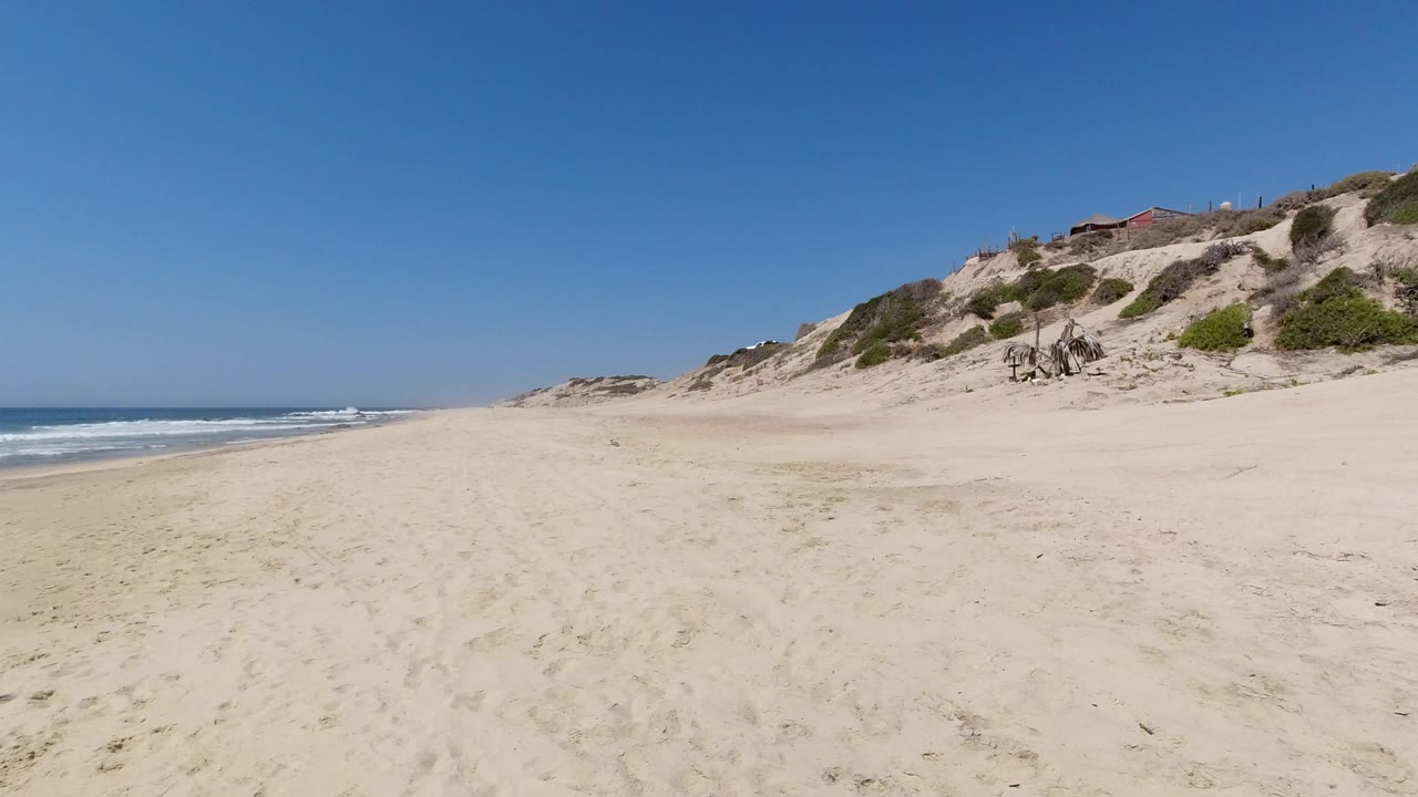 Wide sandy beach with ocean surf and dune-covered hill