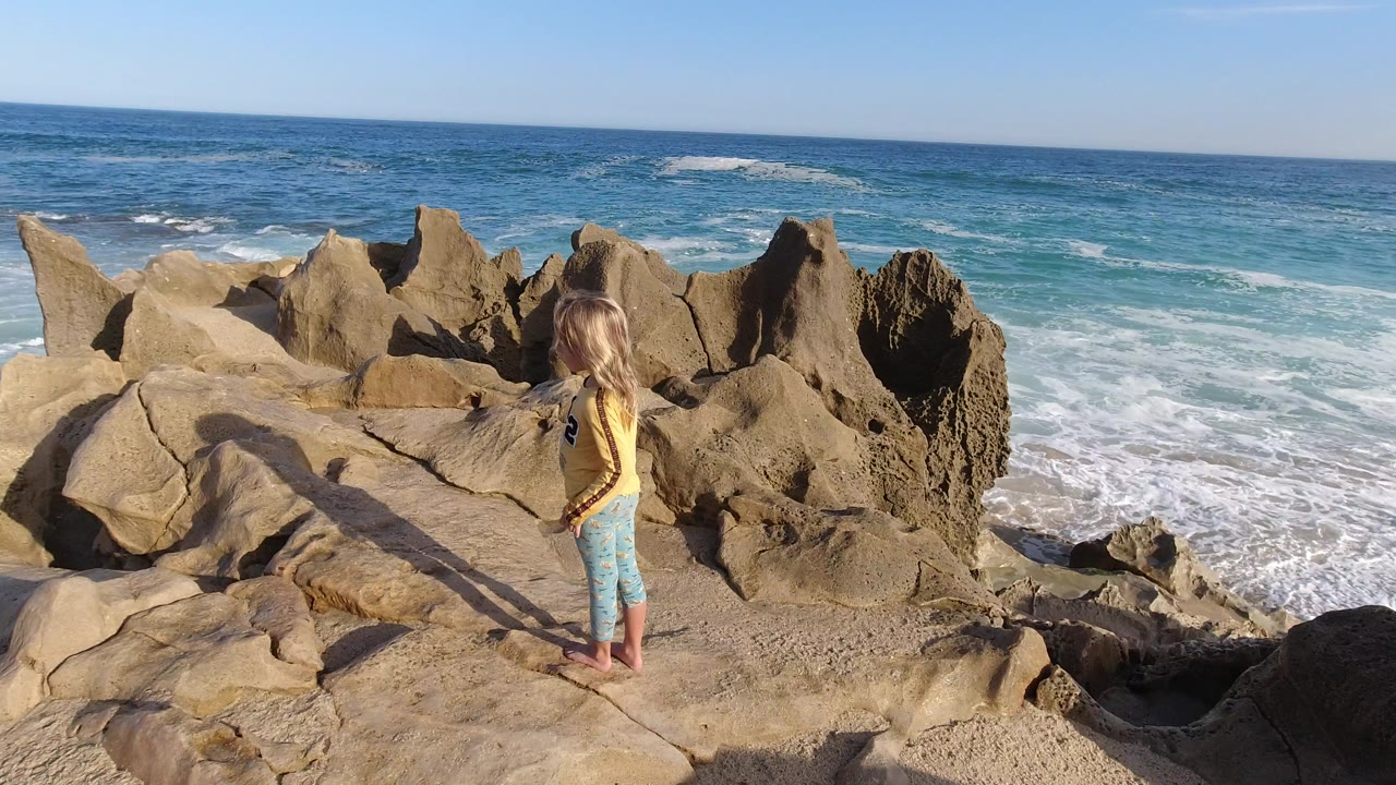 Child standing on rocks above ocean waves.
