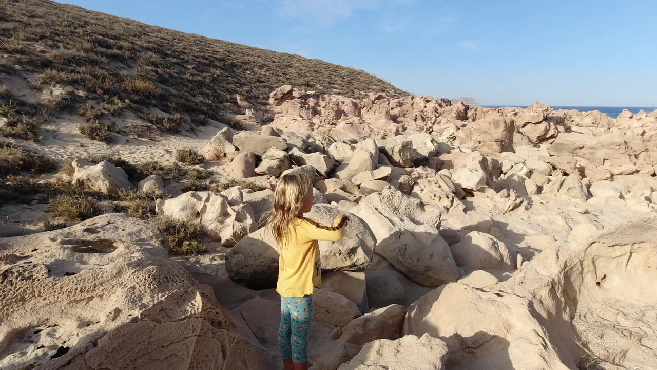 Young girl standing among pale boulders near a scrubby hillside.