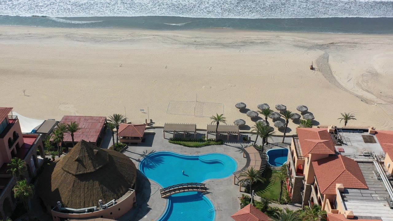 Aerial view of pools beside a sandy beach and ocean surf.