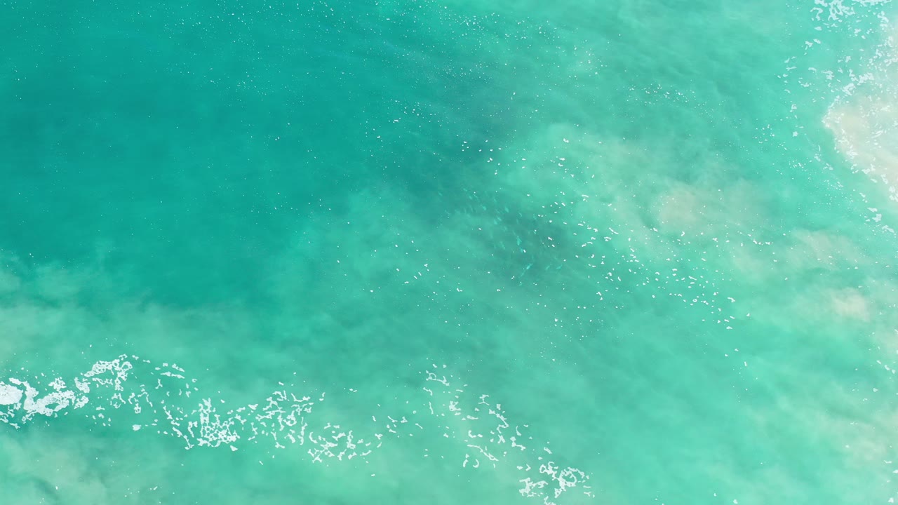 Top-down view of turquoise ocean water in Los Cabos, Mexico, with bright foam along the lower edge and no visible people.