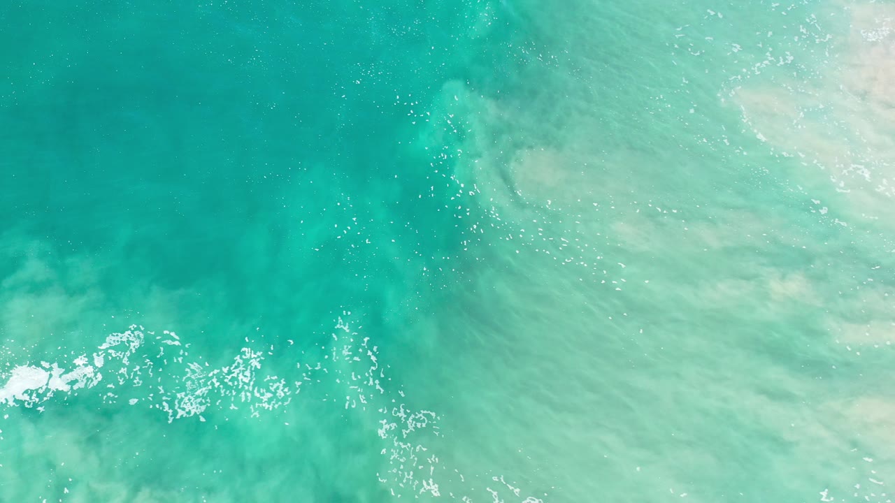 Overhead view of turquoise ocean water in Los Cabos, Mexico with scattered white foam near the lower edge and no visible people.