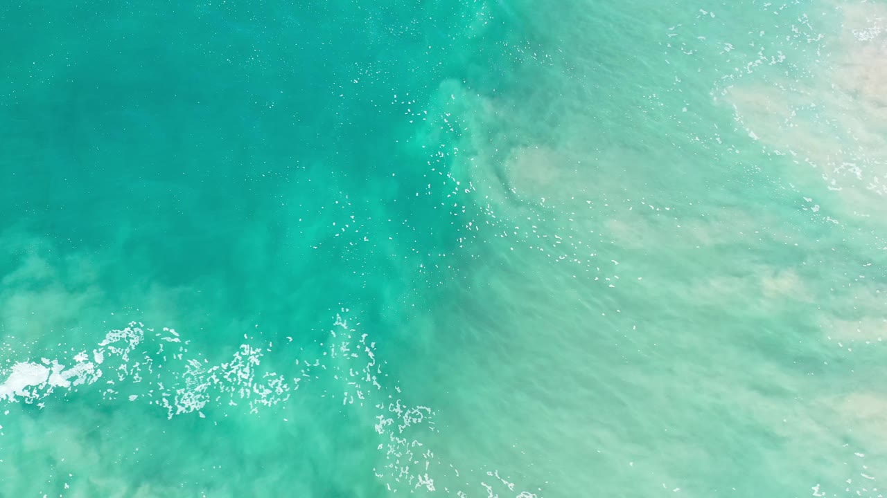 Light green ocean surface in Los Cabos, Mexico with a thin foamy band across the lower frame and no visible people.