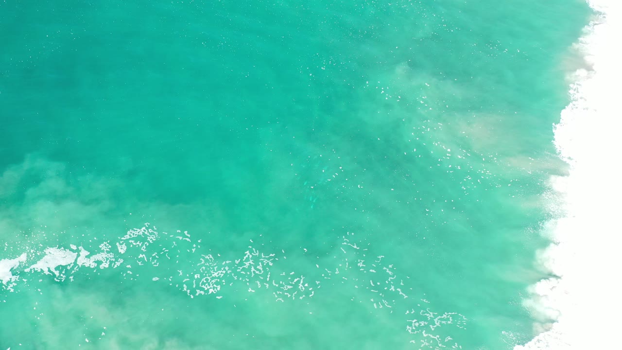 Teal ocean water with white surf foam at the right edge.