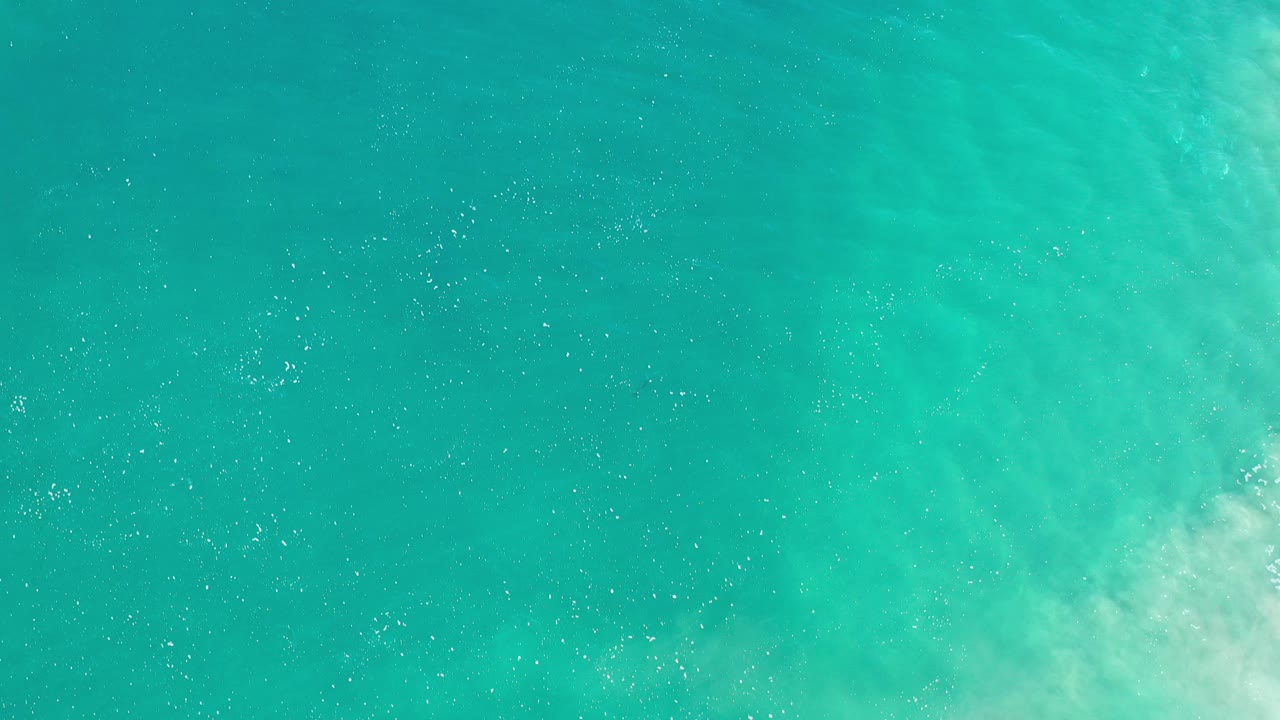 Overhead view of turquoise green ocean water in Los Cabos, Mexico, with scattered white bubbles and no visible people.