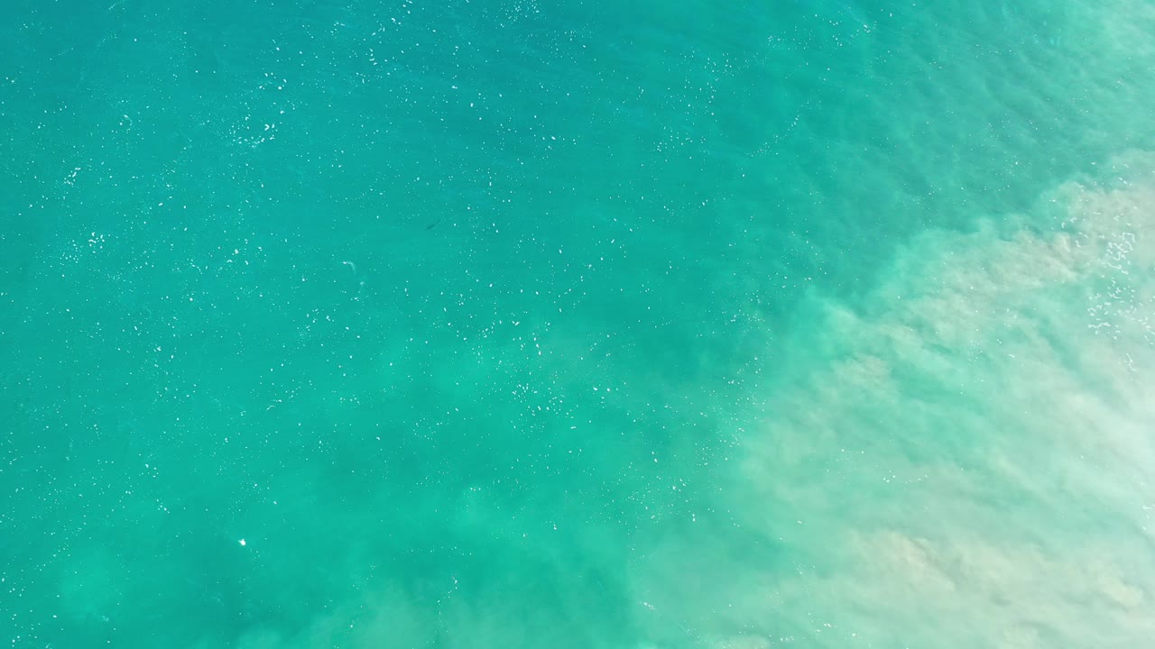 Overhead view of green-blue shallow water in Los Cabos, Mexico, with pale foamy surf entering from the right and no visible people.