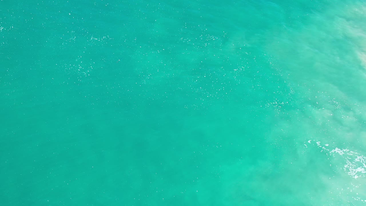 Turquoise ocean water in Los Cabos fills the frame with a pale foamy wave patch near the upper right and no visible people.