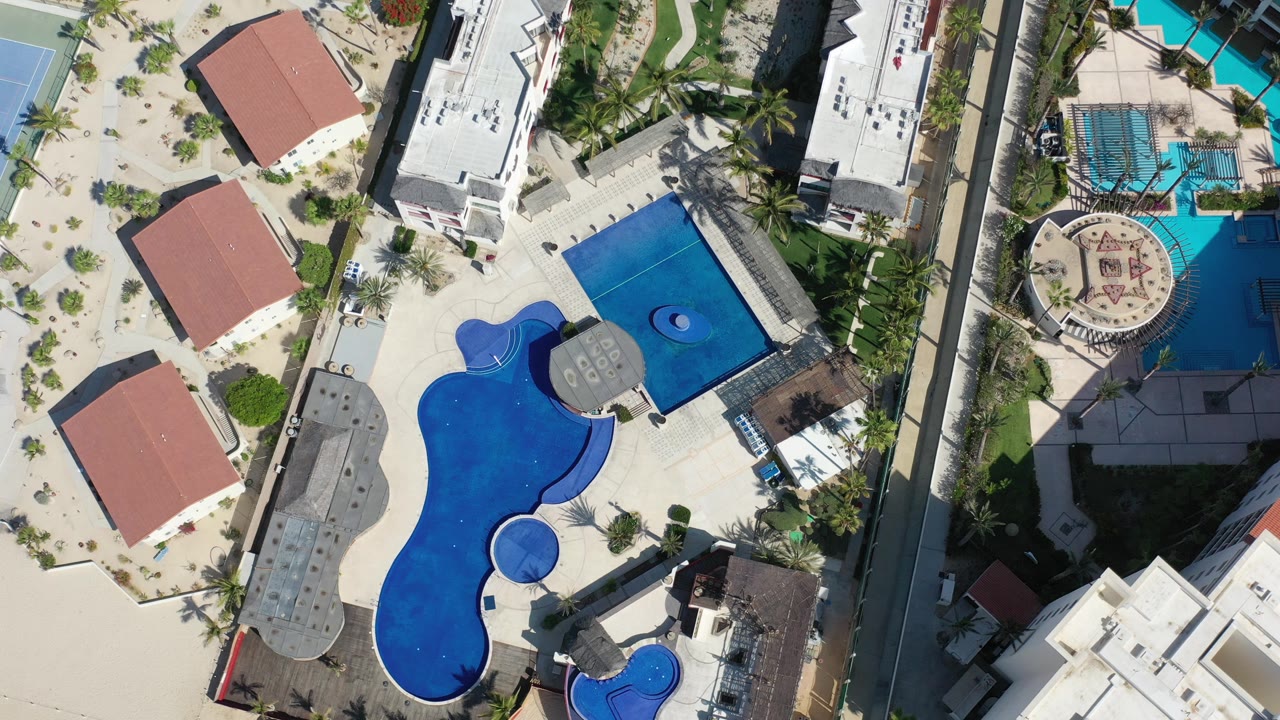 Top-down resort pool complex with red roofs and palm trees.