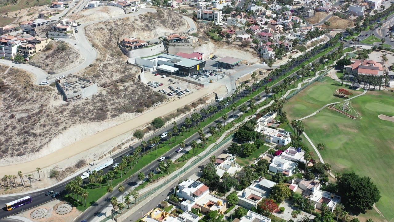 Aerial view of dry hills, green lawns, homes, and a highway.