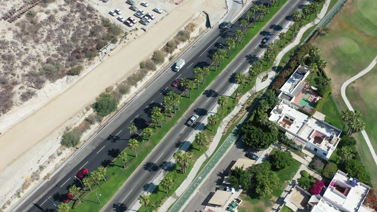 Overhead view of a road beside sandy dunes and green landscaping.